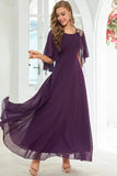 Woman in long purple dress with sheer cape sleeves and gold shoulder embroidery standing indoors | PicSEO 1787445918679
